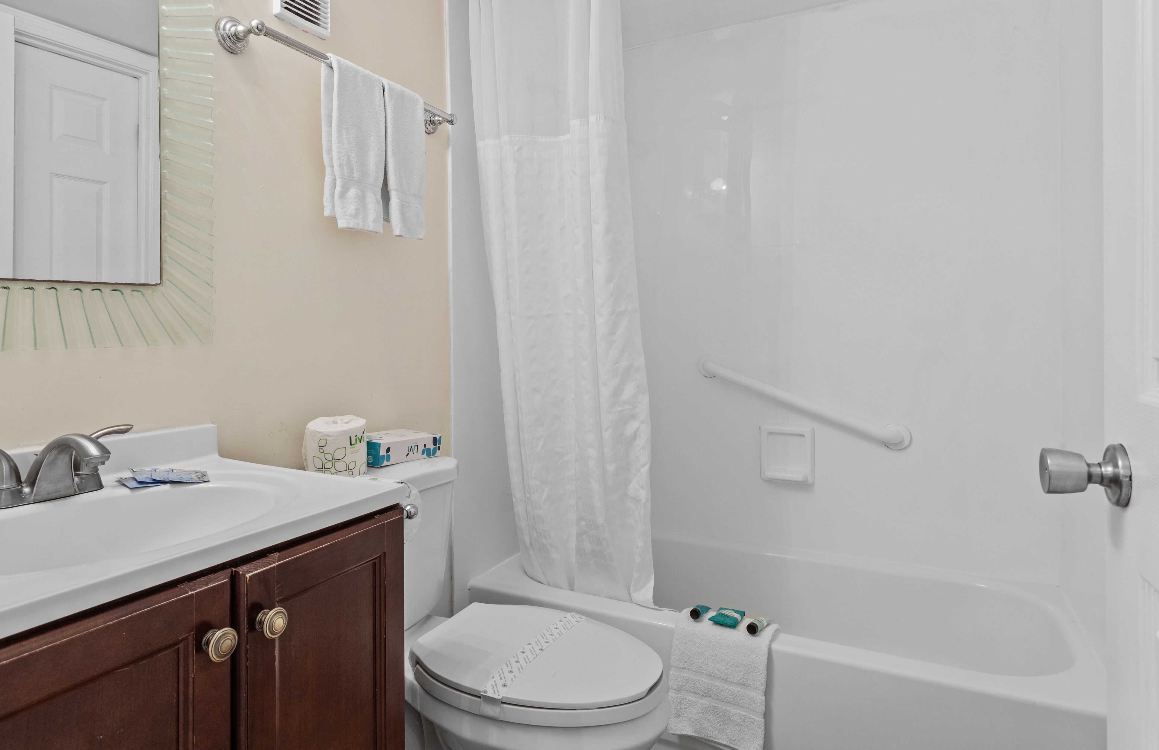 A bathroom with a white sink, toilet, and bathtub. There is a shower curtain, a towel rack, and a mirror.