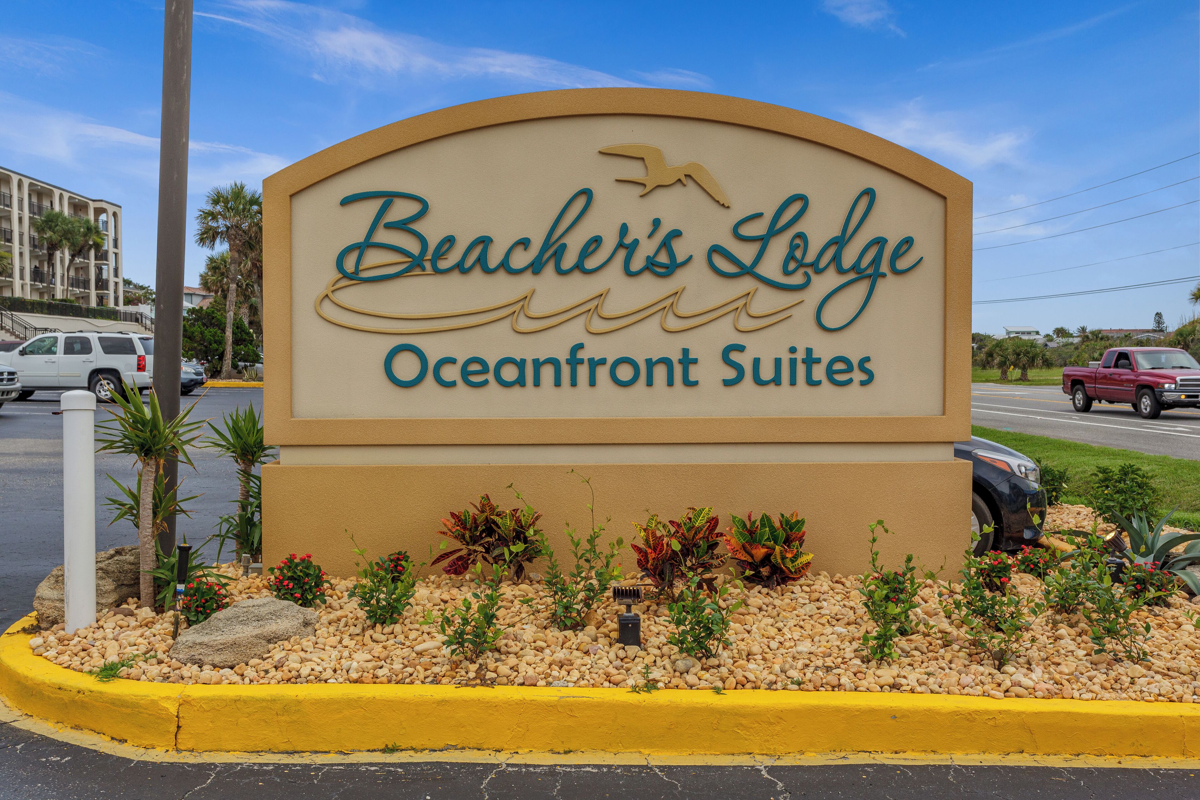 Señal de Beacher's Lodge Oceanfront Suites con una vista despejada del entorno, incluyendo automóviles estacionados y un edificio al fondo.