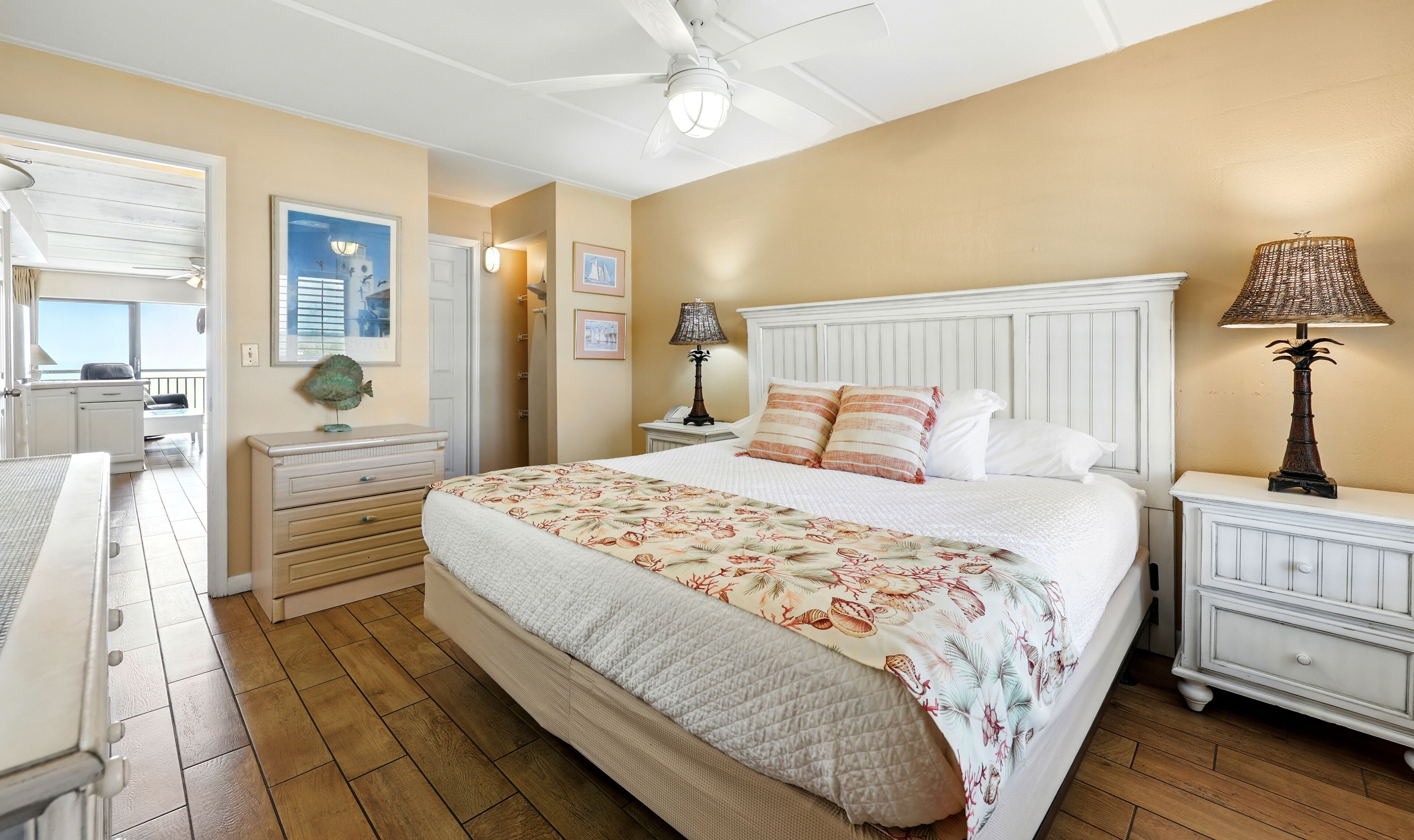 A bedroom with a large bed, a nightstand with a lamp, a dresser, and a window with blinds.
