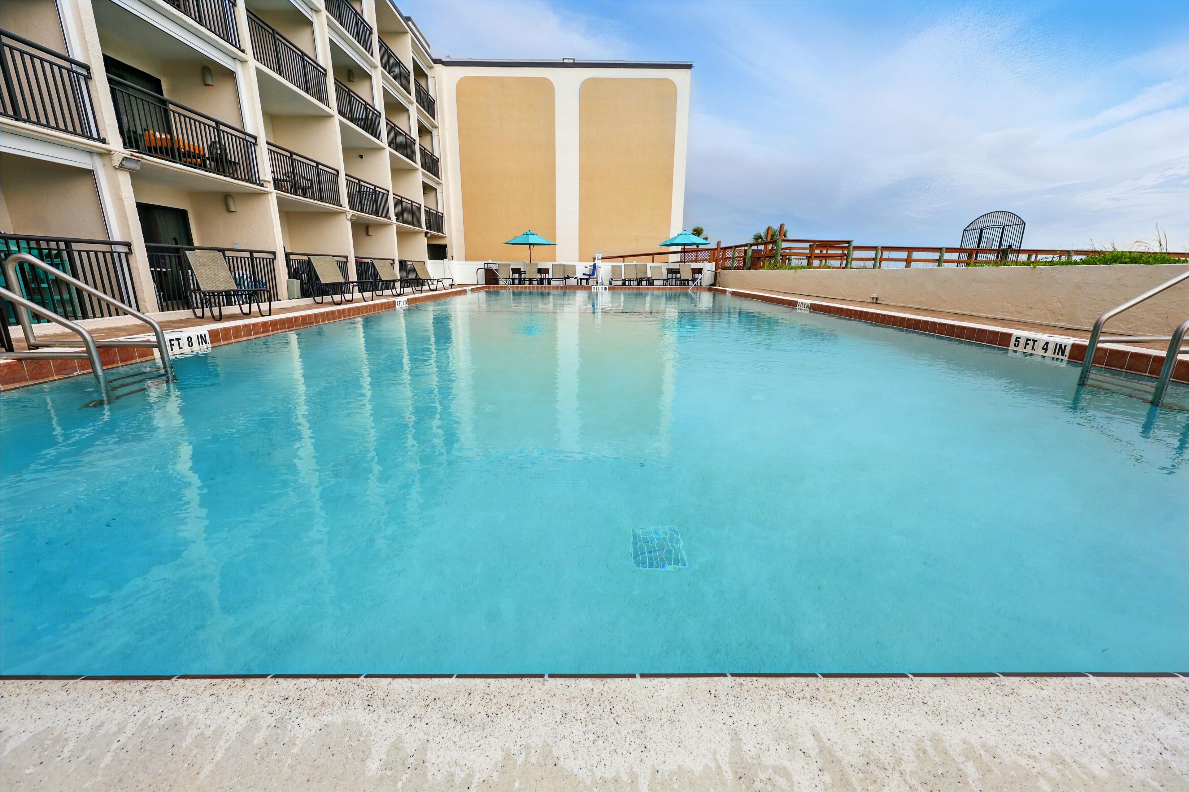 A swimming pool with a clear blue water, surrounded by a poolside area with lounge chairs and umbrellas.