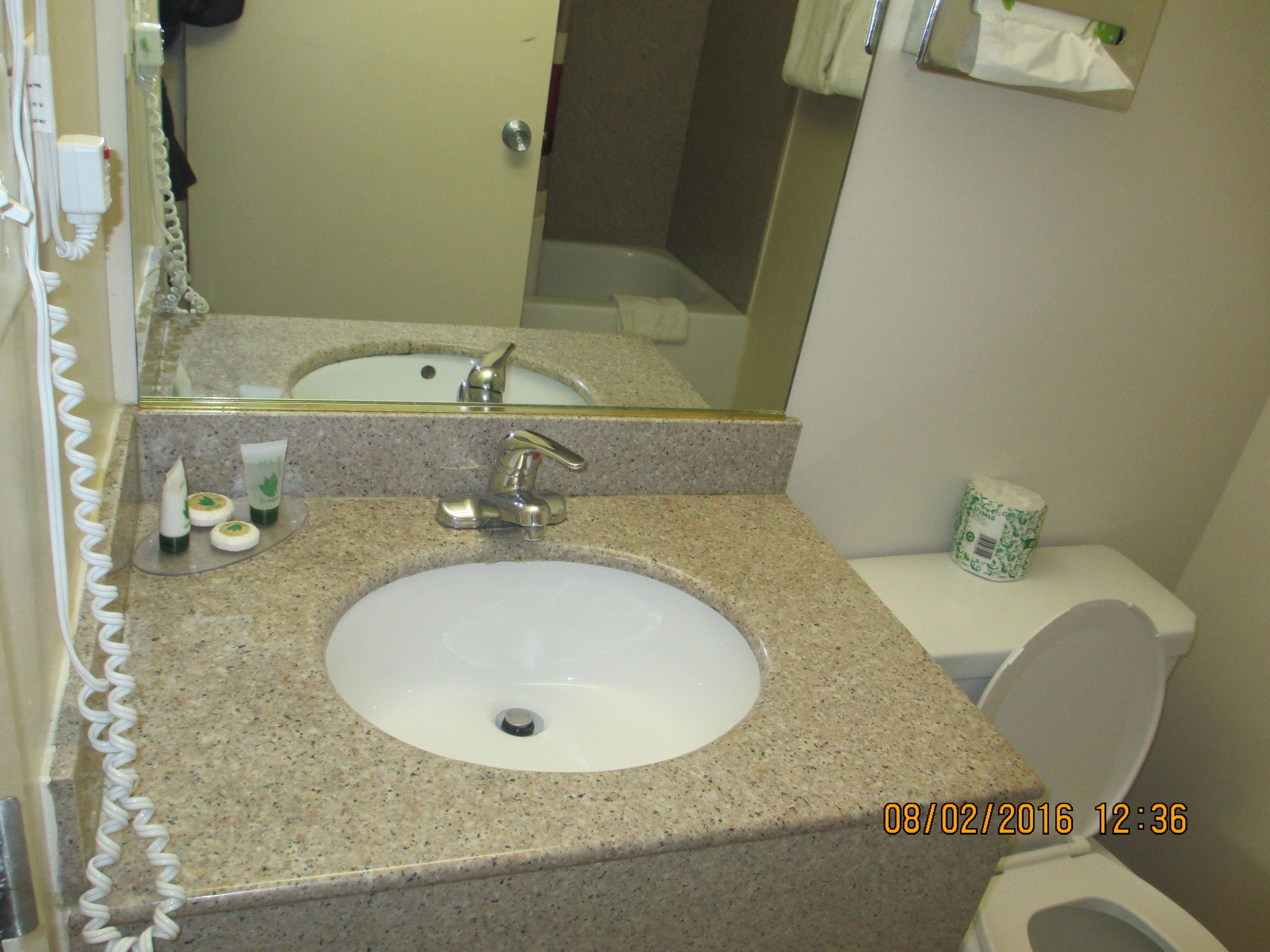 A bathroom with a granite countertop sink, a mirror above it, and a toilet with a paper towel holder.