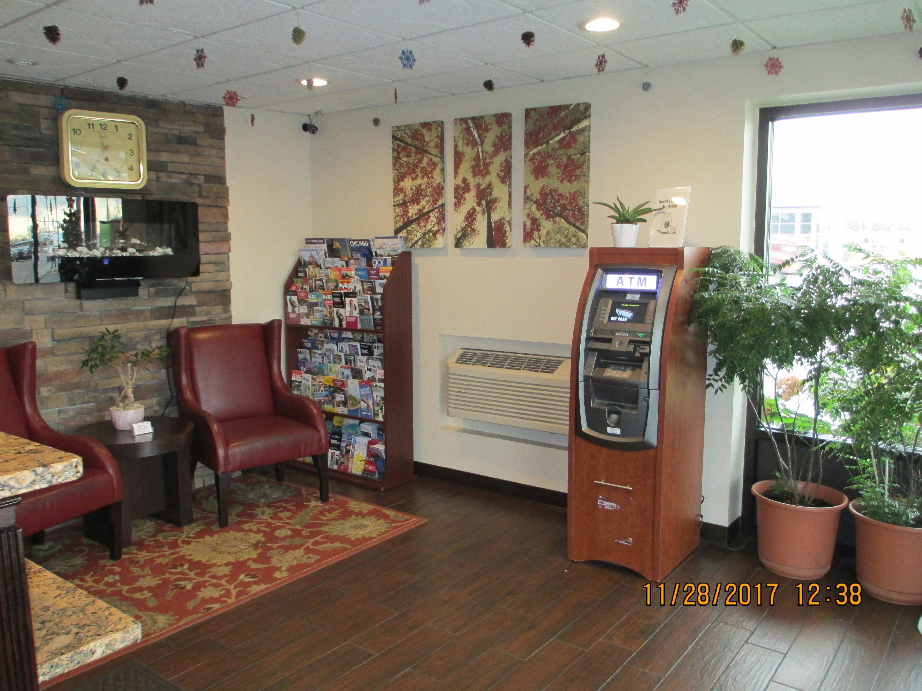 A lobby with a reception desk, a red leather chair, a wall-mounted clock, a wall-mounted ATM, and a potted plant.