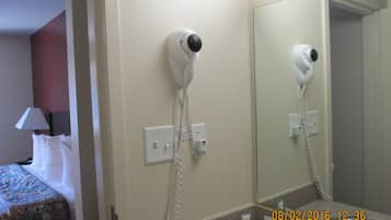 Une chambre d’hôtel équipée d’un lit, d’un sèche-cheveux fixé au mur, d’un miroir et d’un lavabo avec des articles de toilette.