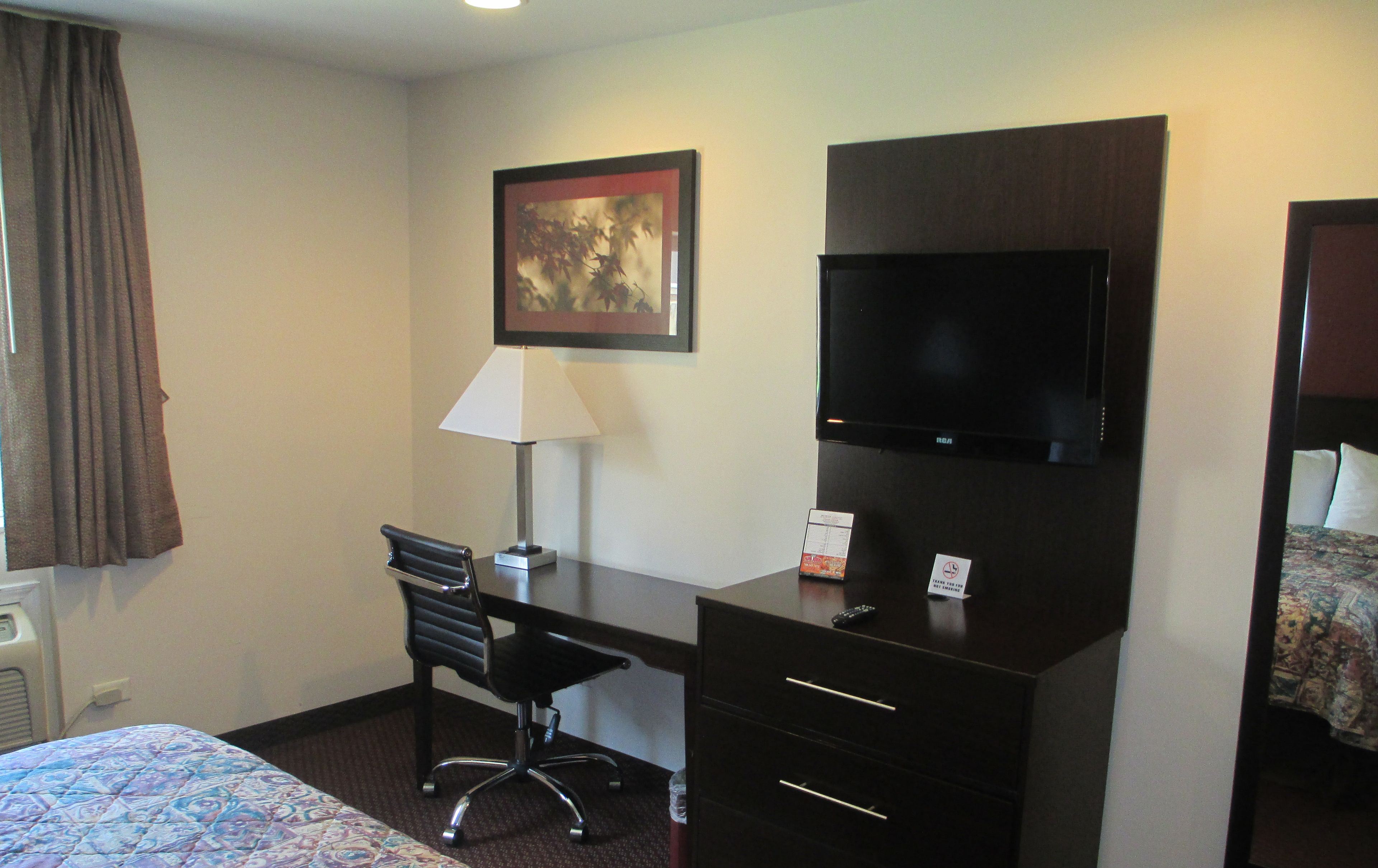 A hotel room with a bed, a desk with a chair, a television, and a painting on the wall.