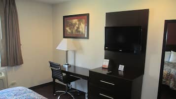 A hotel room with a bed, a desk with a chair, a television, and a painting on the wall.