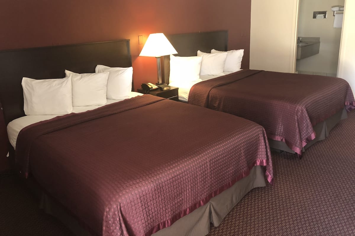 A hotel room with two beds, a nightstand with a lamp, and a bathroom visible through an open door.