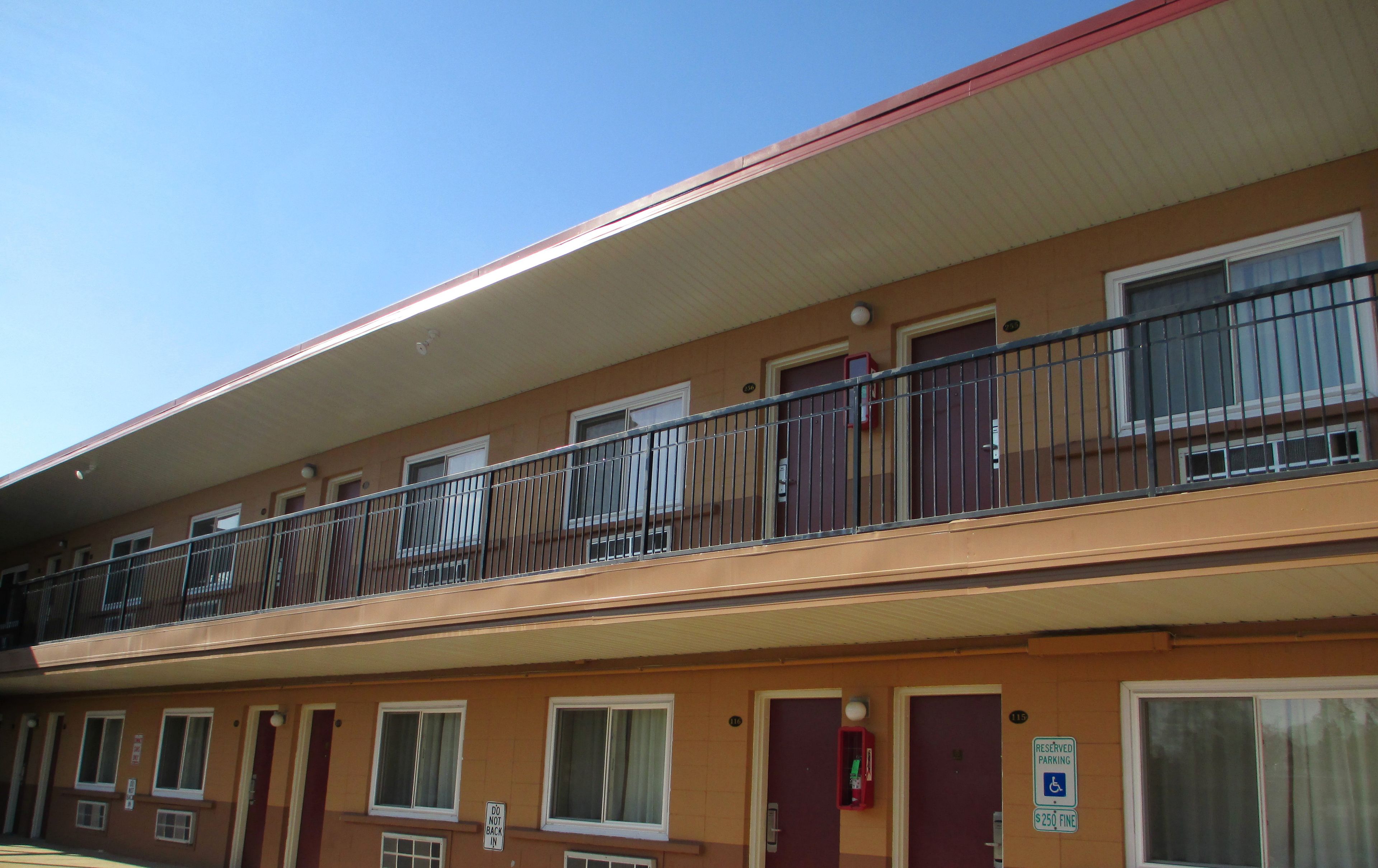 A multi-story motel with a red roof, balconies with metal railings, and a reserved parking sign.