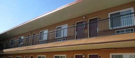 A multi-story motel with a red roof, balconies with metal railings, and a reserved parking sign.