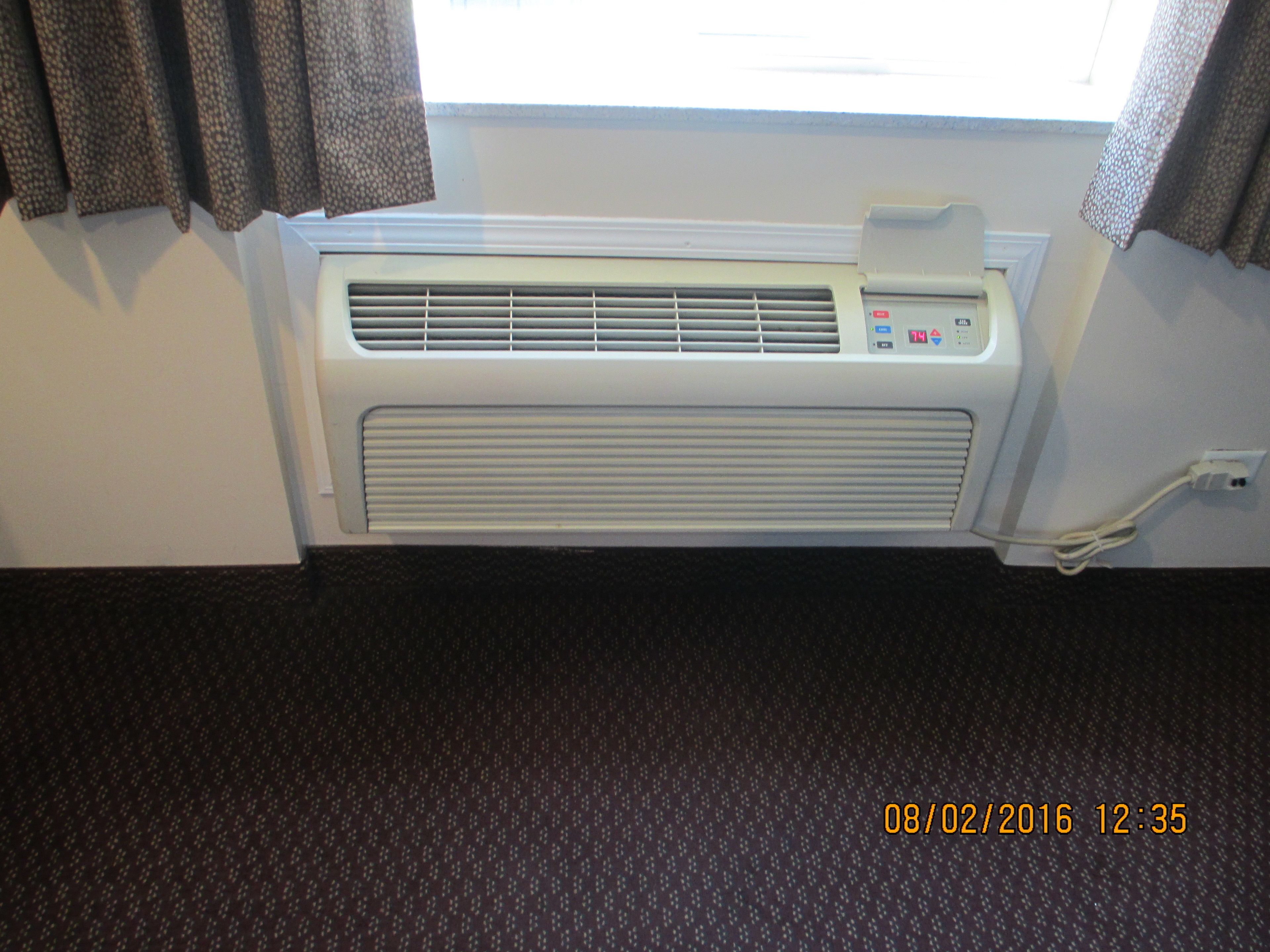A room with a window, a wall-mounted air conditioner, and a carpeted floor.