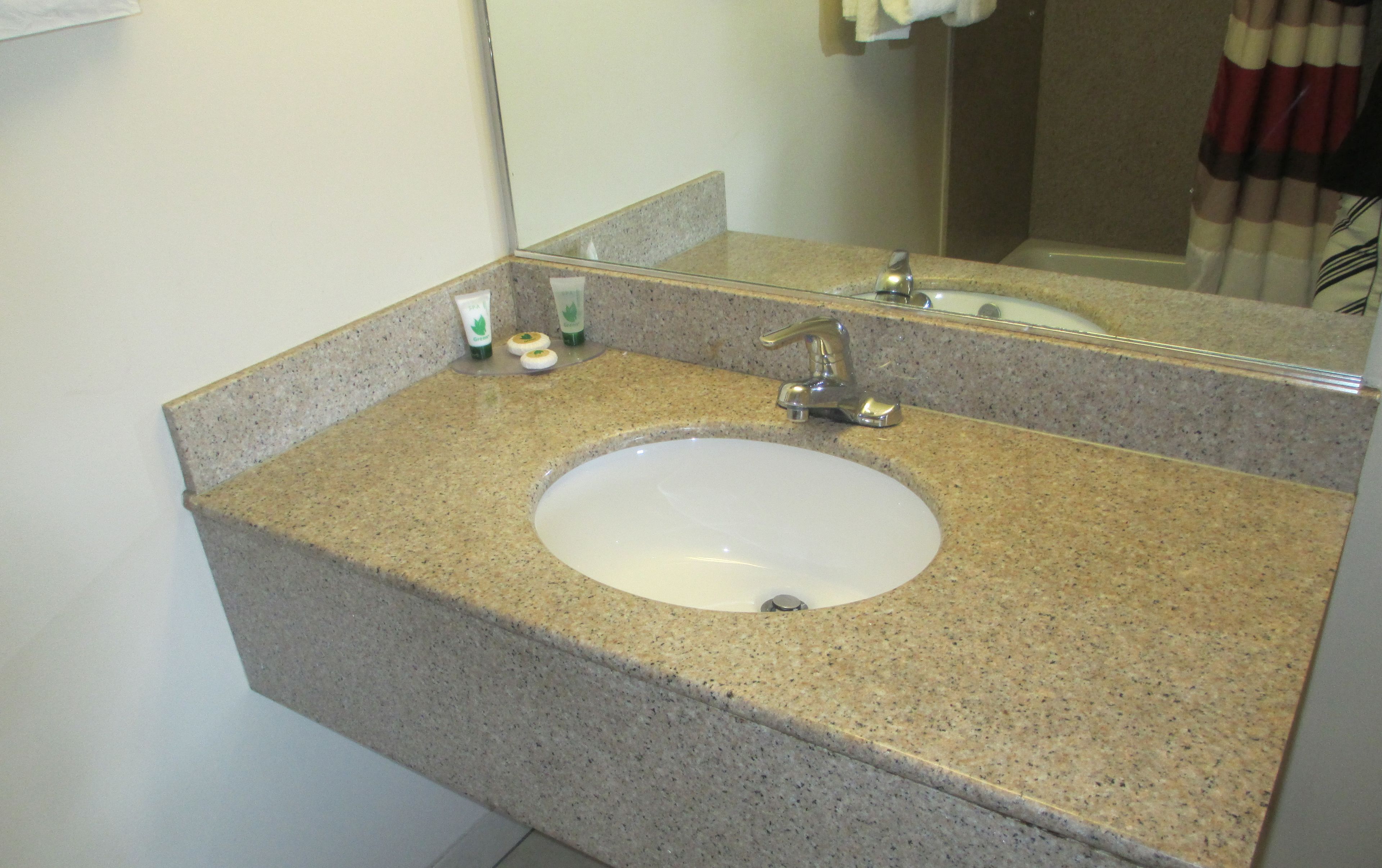 A bathroom with a granite countertop, a white sink, and a mirror.