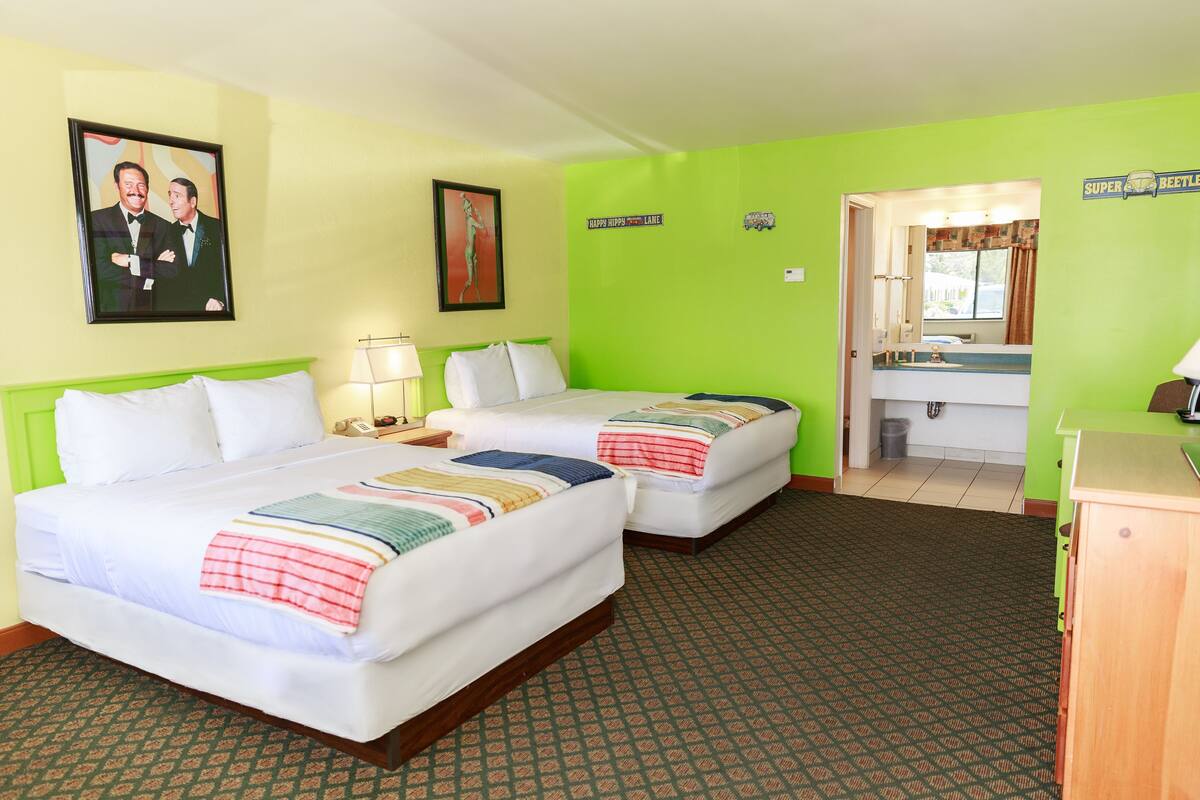 A hotel room with two beds, a bathroom, and a green wall.