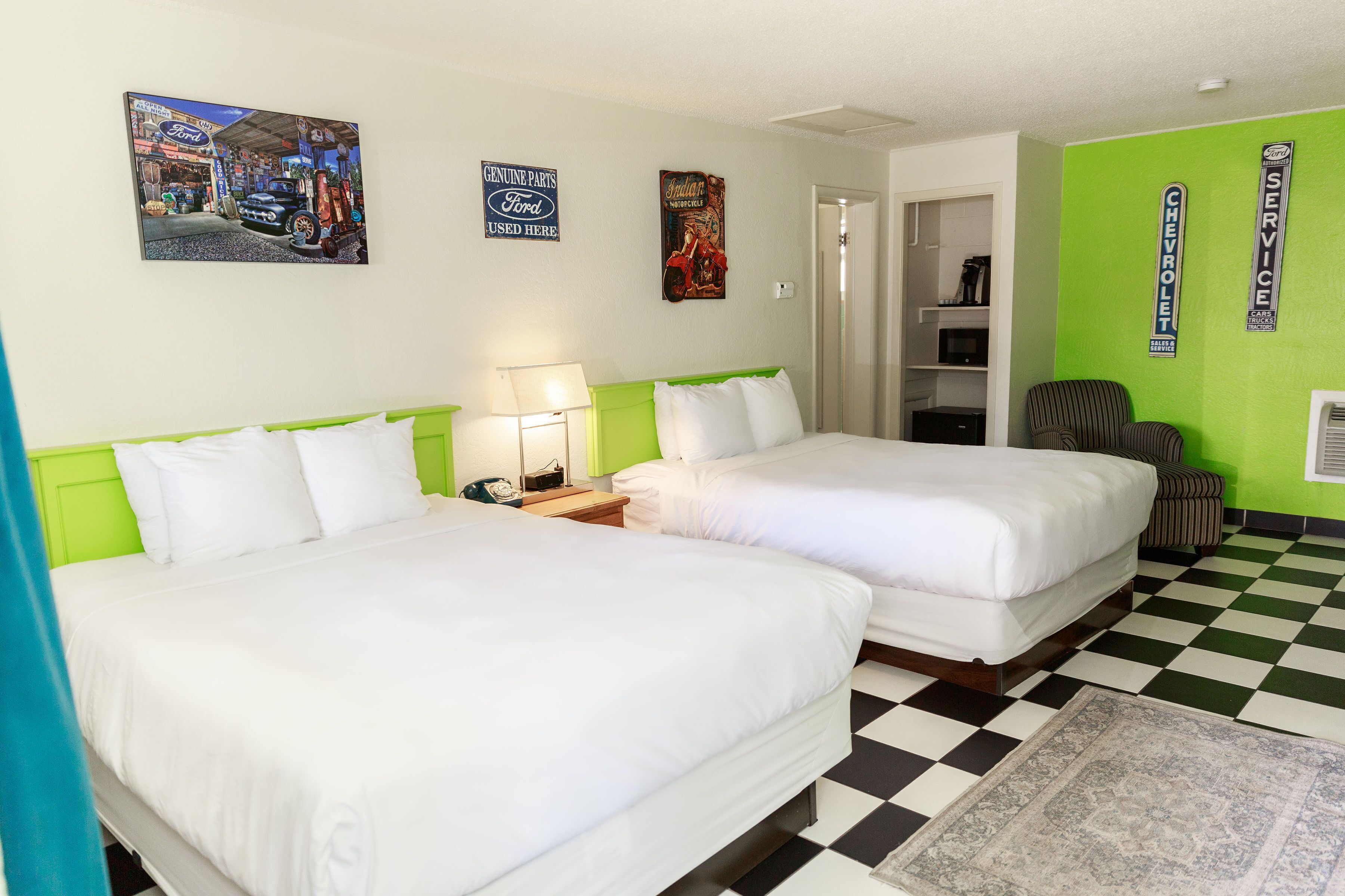 Habitación de hotel con dos camas, piso a cuadros y decoraciones en la pared que incluyen carteles de automoción.