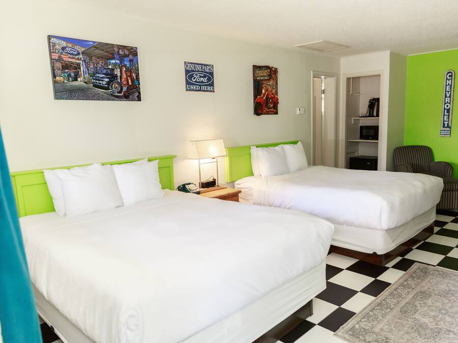 Habitación de hotel con dos camas, piso a cuadros y decoraciones en la pared que incluyen carteles de automoción.