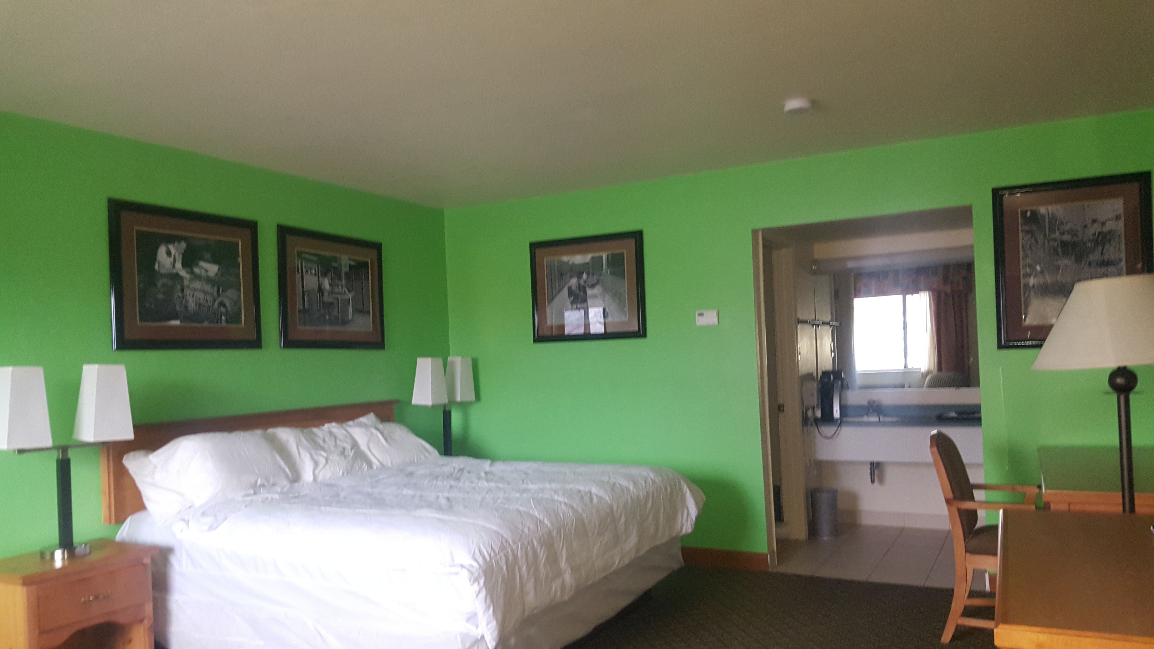 A hotel room with a bed, two bedside tables with lamps, a wooden chair, and a desk with a lamp. There are three framed pictures on the wall.