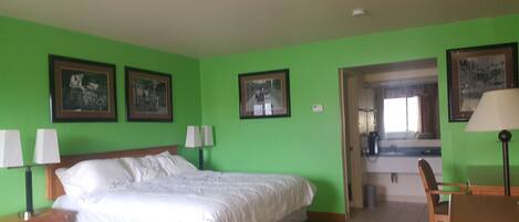 A hotel room with a bed, two bedside tables with lamps, a wooden chair, and a desk with a lamp. There are three framed pictures on the wall.
