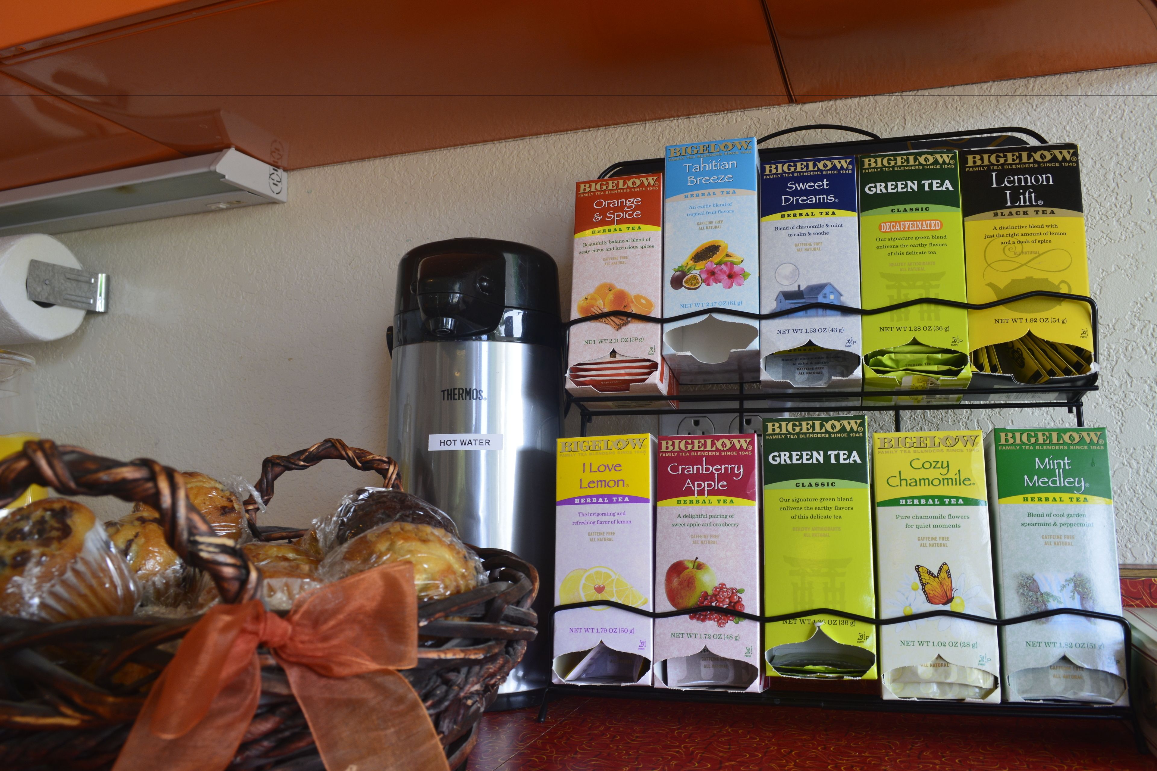 A kitchen counter with a coffee maker, a basket of bread, and a rack of tea boxes.