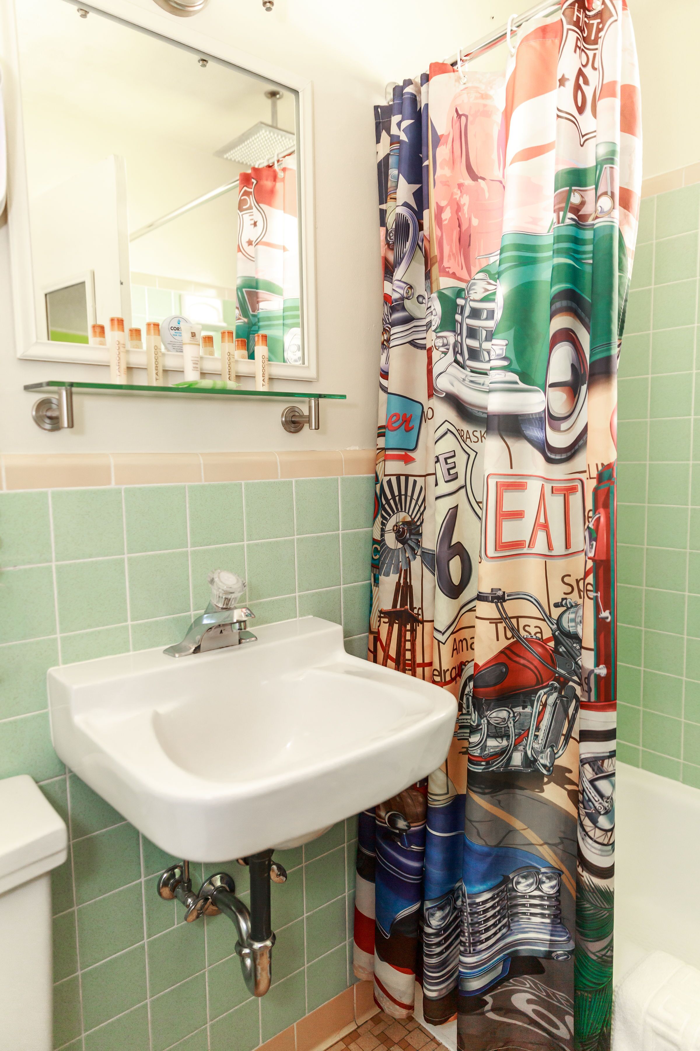 Bagno con lavandino bianco, piastrelle verdi e tenda della doccia con un design di auto d'epoca e food truck.