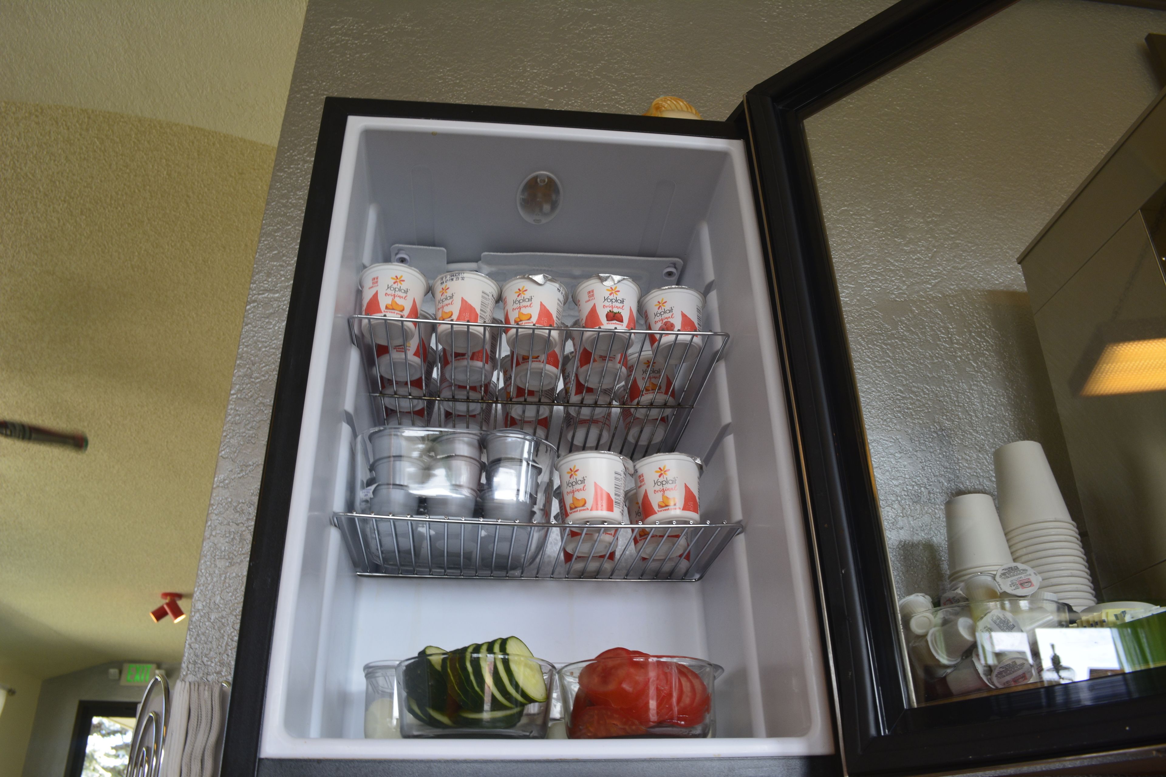 Un réfrigérateur avec des étagères contenant des pots de yaourt, des briques de jus de fruits et quelques légumes.