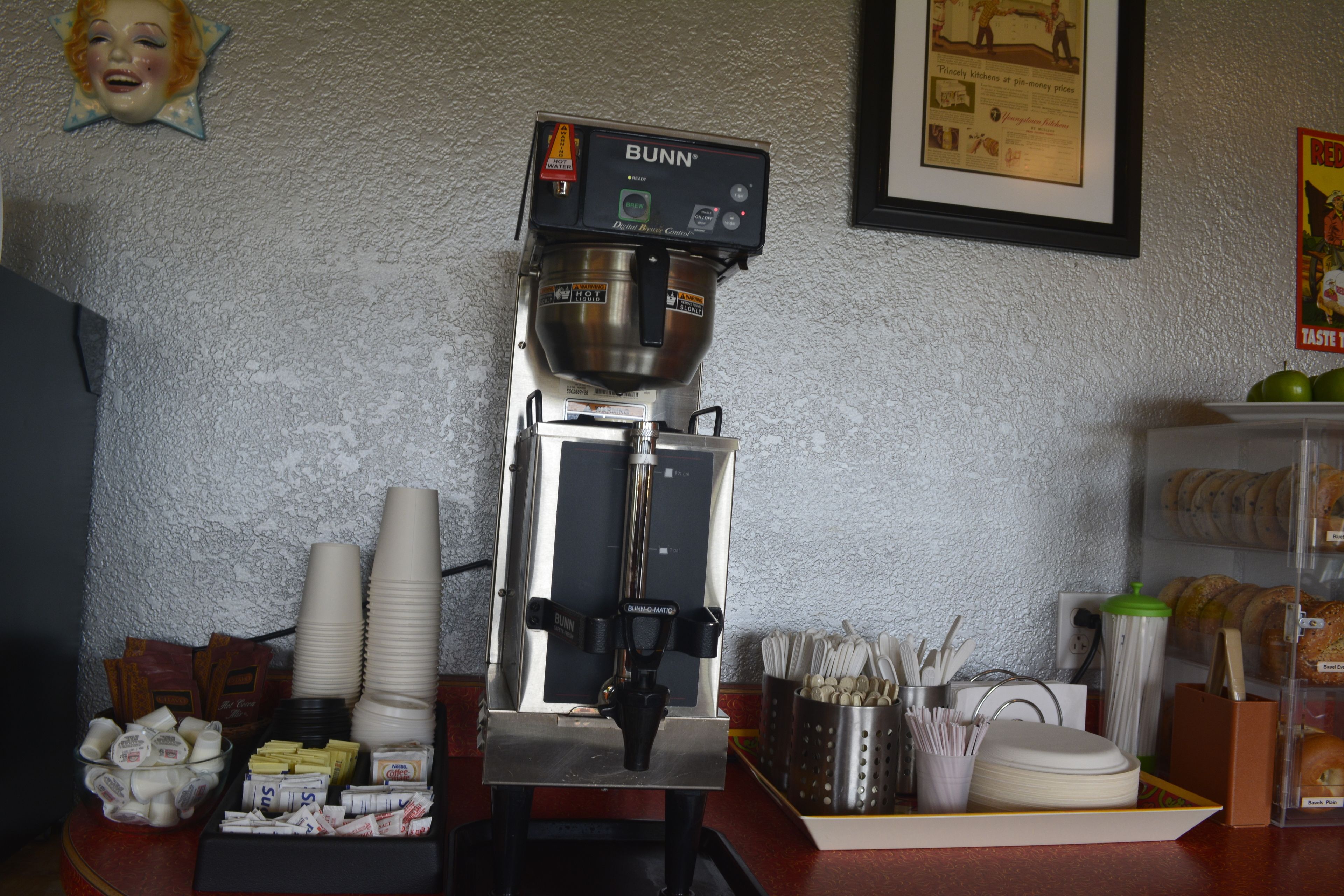Una máquina de café con la etiqueta de marca Bunn, una pila de tazas blancas y un recipiente con cápsulas de café.