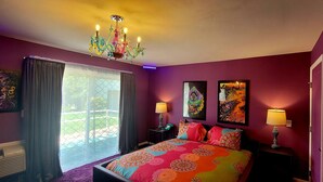 Une chambre à coucher avec une couvre-lit aux couleurs vives, un lustre et des œuvres d’art accrochées aux murs.