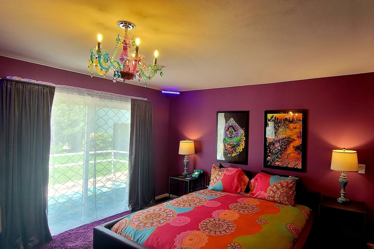 A bedroom with a colorful bedspread, a chandelier, and artwork on the walls.
