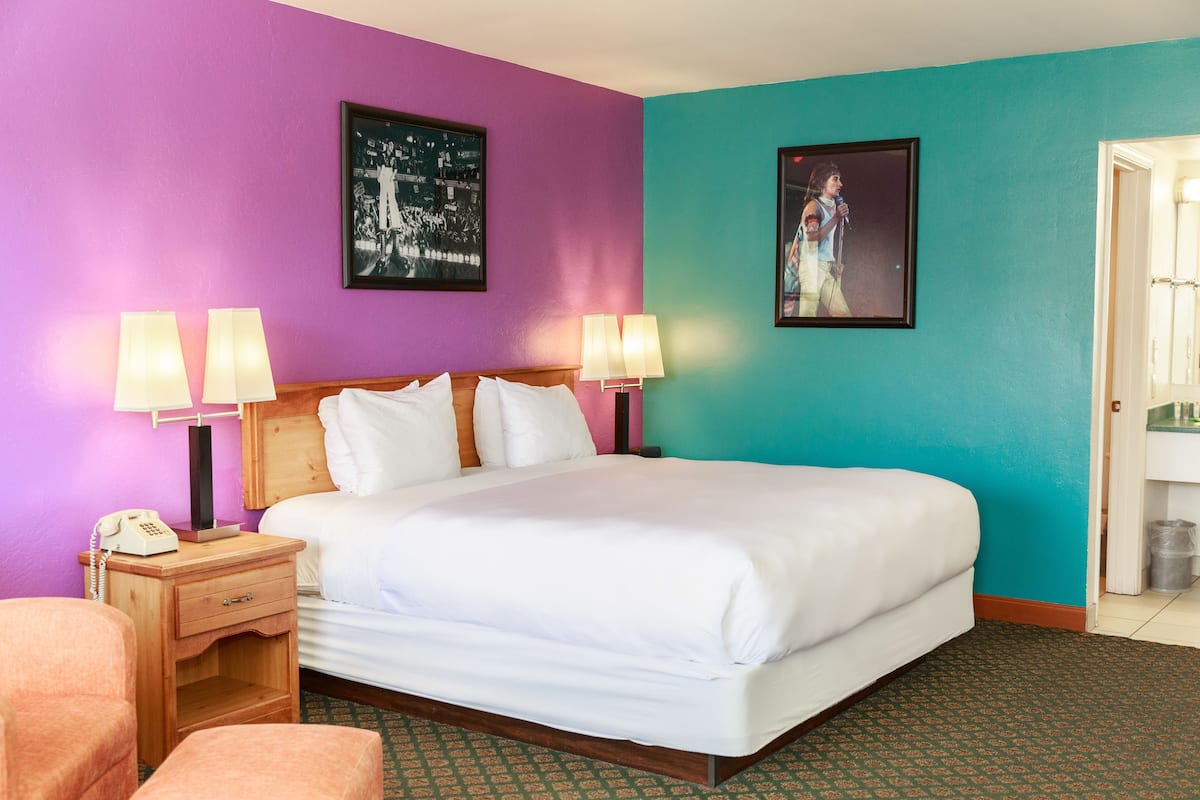 A hotel room with a bed, two bedside lamps, a nightstand with a phone, and two framed pictures on the walls.