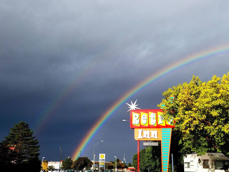 Segnale di un hotel con un arcobaleno, alberi e una stazione di servizio Shell sullo sfondo.
