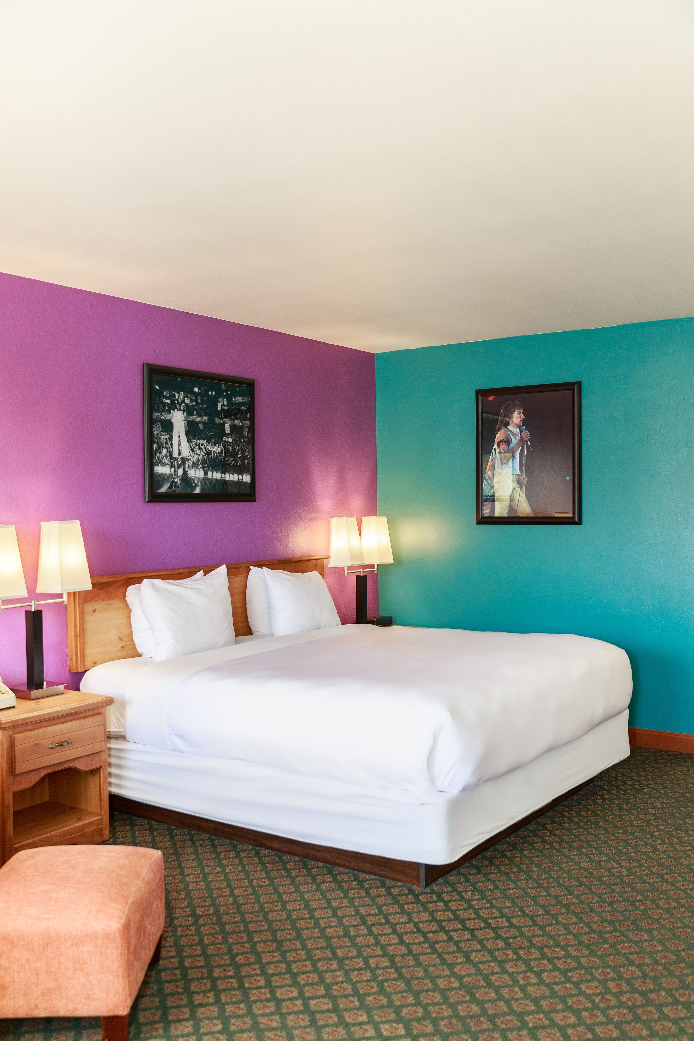 Habitación de hotel con una cama grande, dos mesitas de noche con lámparas, un tocador de madera, un banco y dos cuadros enmarcados en las paredes.