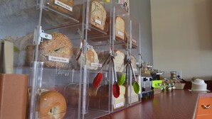 Une vitrine de boulangerie présentant différents types de pains et de viennoiseries, notamment des bagels et des muffins, avec des étiquettes pour faciliter leur identification.