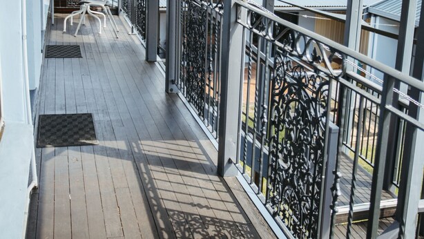 A covered balcony with a wooden floor, metal railing, and a table with chairs. - Colonial Motel Richmond (Richmond)