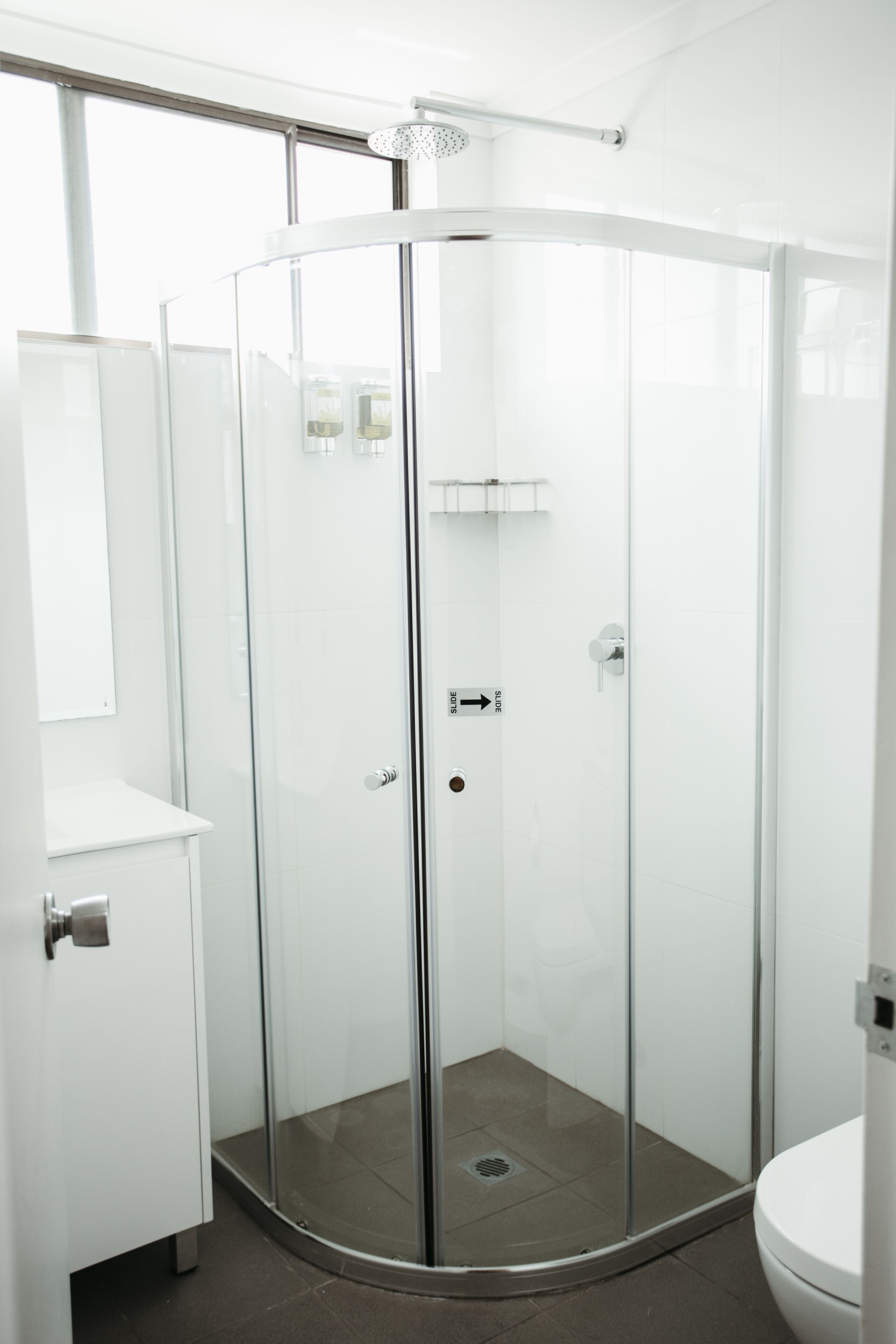 Un bany modern amb plat de dutxa envoltat de vidre, un lavabo blanc i un vàter.