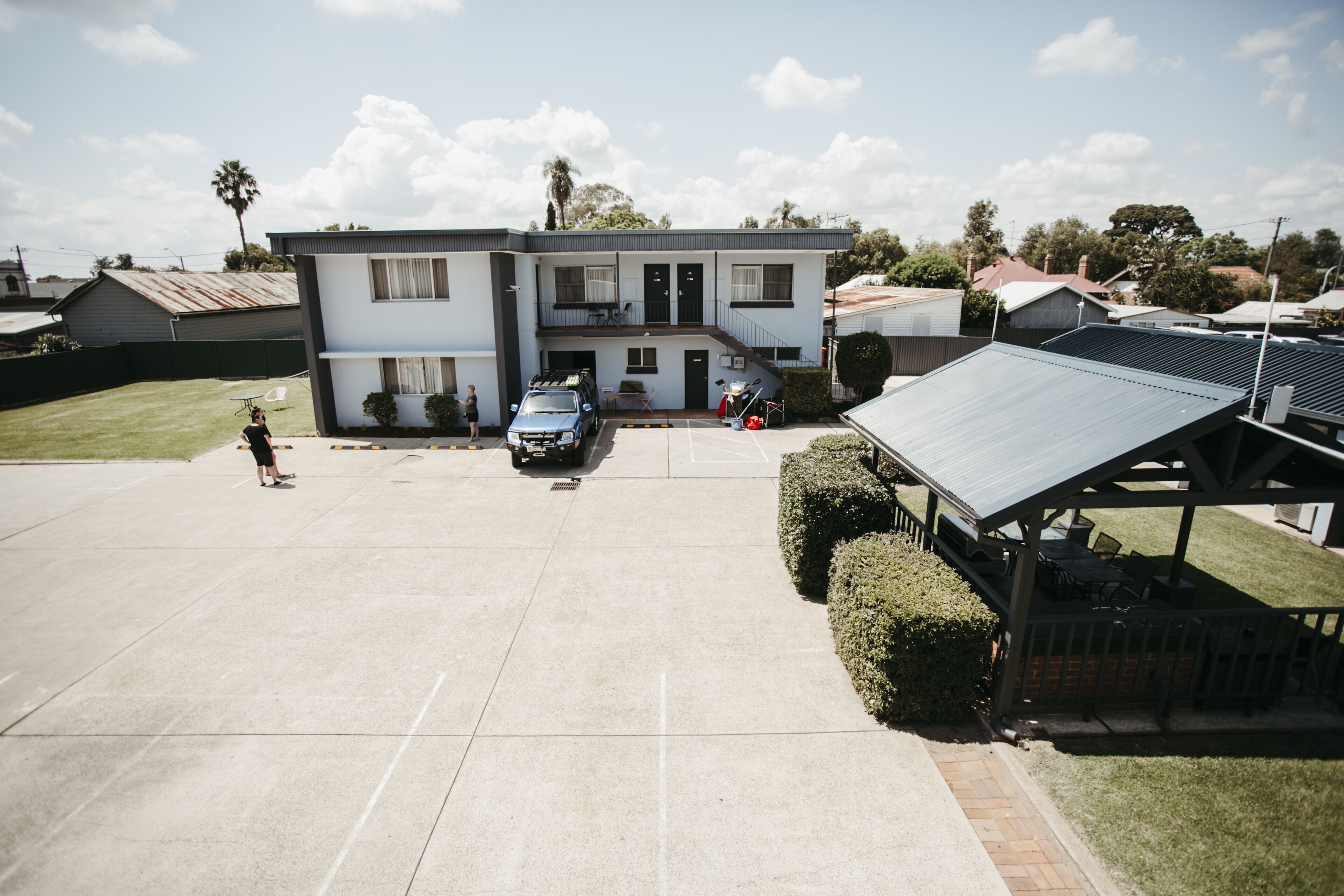 Un bâtiment à deux étages, doté d’un toit plat, d’un espace extérieur abrité avec des sièges et d’un parking.