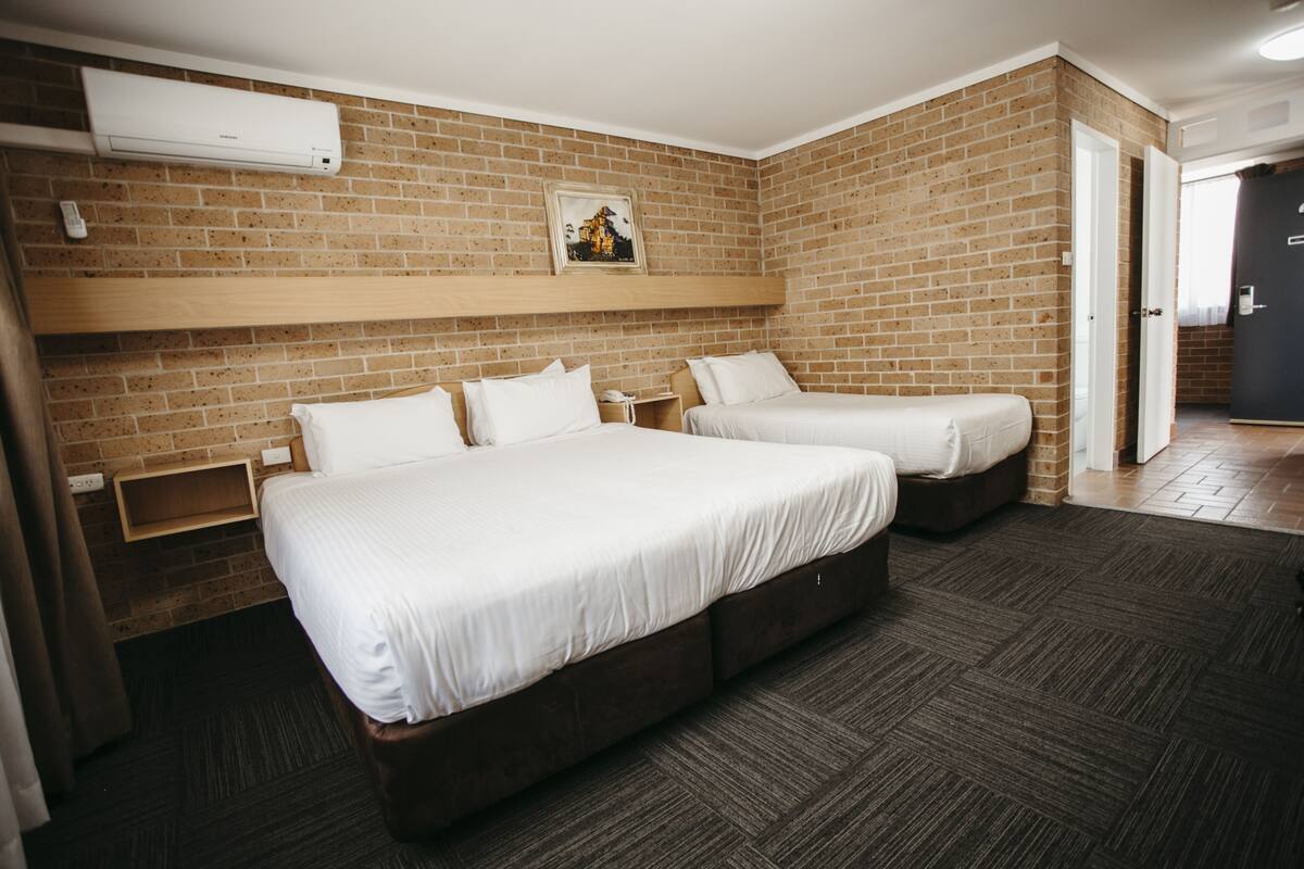 A hotel room with two beds, a brick wall, and a wooden headboard.