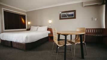 Habitación de hotel con cama, una mesa con sillas, un banco y un cuadro colgado en la pared.