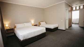 A hotel room with two single beds, a nightstand with a lamp, and a door leading to another room.
