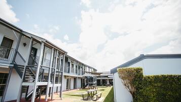 A courtyard with a building featuring multiple balconies and a staircase. There are picnic tables and a small lawn area.