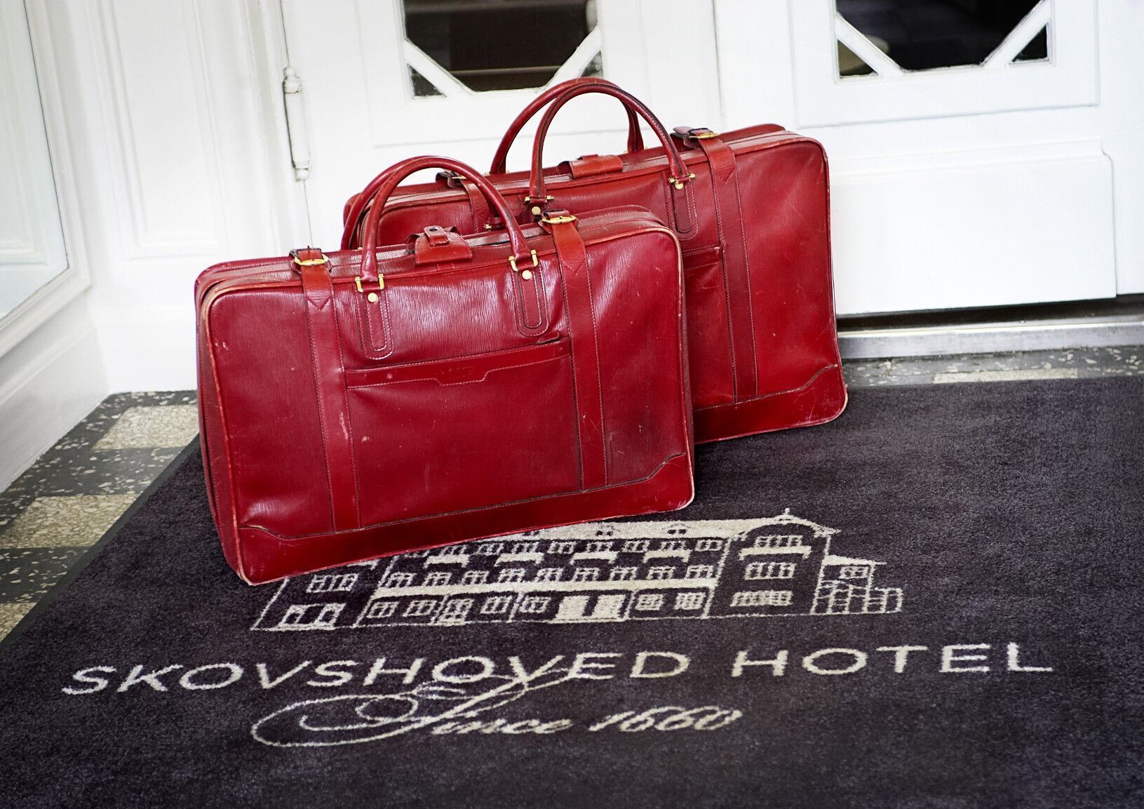 Two red leather bags on a doormat with the text "KOVSHORED HOTEL Since 1860".