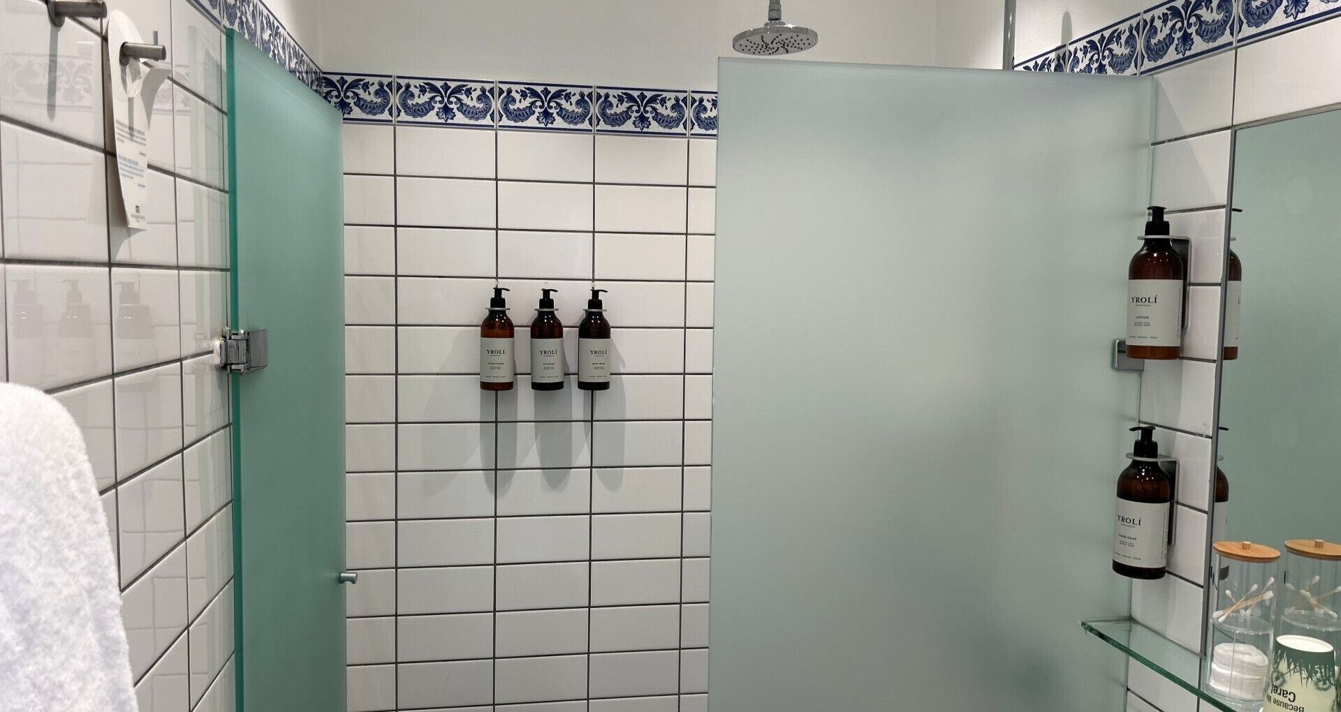 Casa de banho com azulejos brancos, porta verde e produtos de higiene pessoal nas prateleiras.