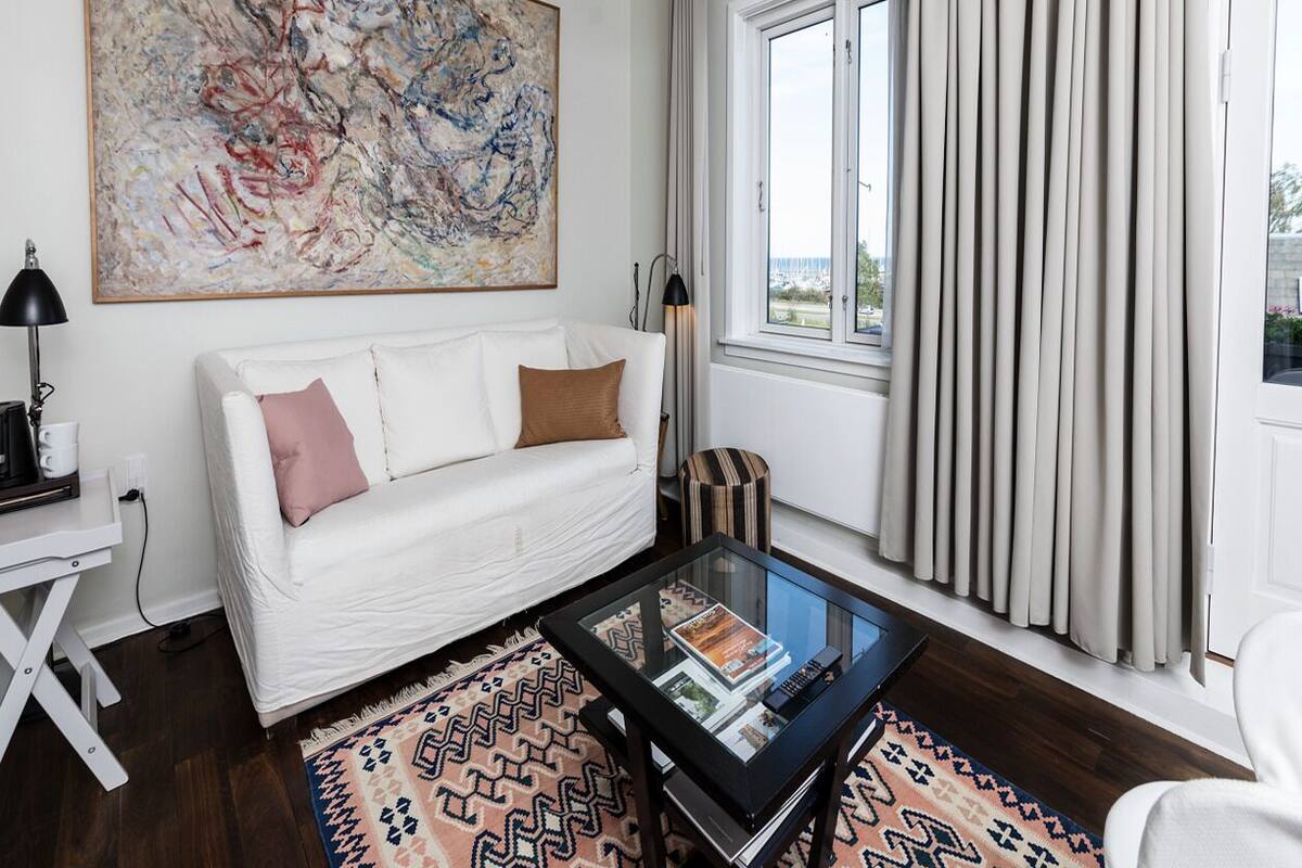 Una sala de estar moderna con un sofá blanco, una mesa de centro de cristal, un tapete estampado y un cuadro abstracto grande en la pared.