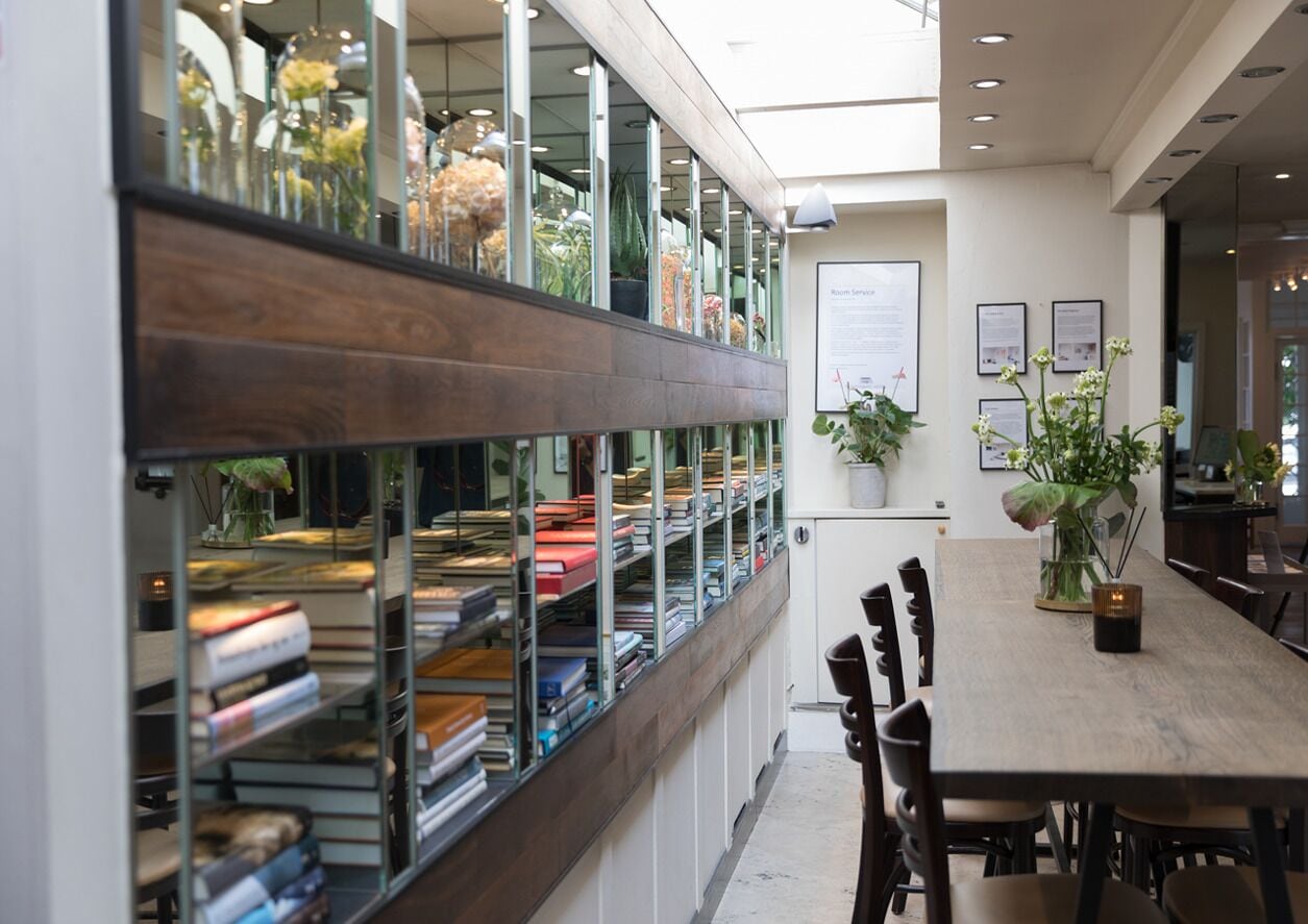 A modern library with bookshelves, a wooden table, and potted plants.