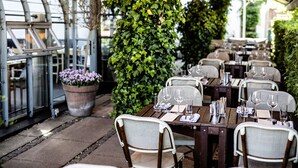 An outdoor restaurant with tables set for dining, surrounded by greenery and a glass structure. - Skovshoved Hotel (Charlottenlund)