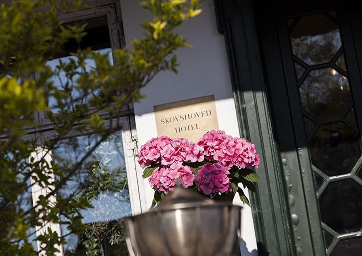 A sign for the Skovshoved Hotel with a large metal pot of pink flowers in front.