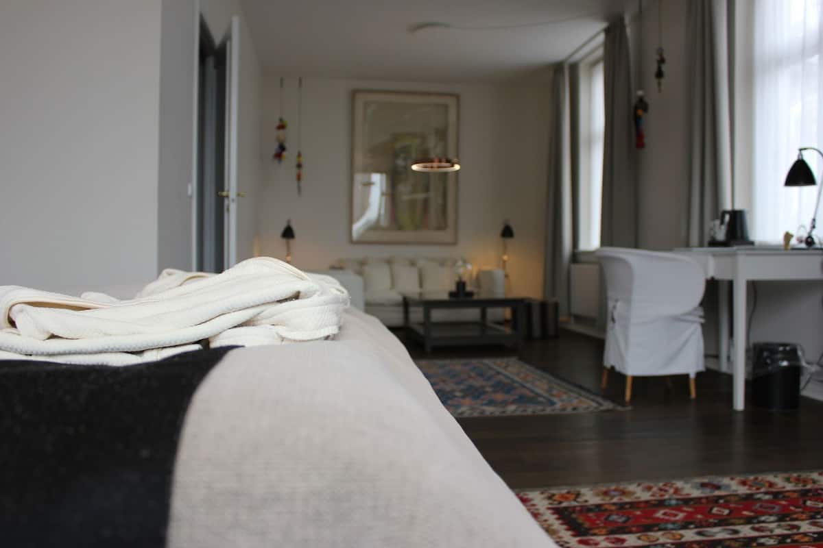 Un dormitorio con cama, escritorio, silla, alfombra y lámpara colgante.