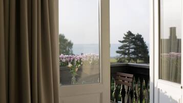 A balcony with a view of the sea, a chair, and a window with flowers.