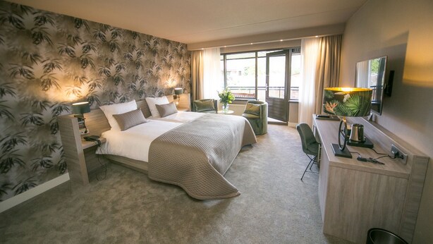 A hotel room with a large bed, a desk, a chair, a TV, and a window with curtains.