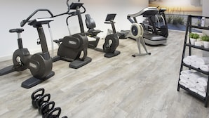 A gym with various exercise machines, a wall mural, and neatly arranged towels.