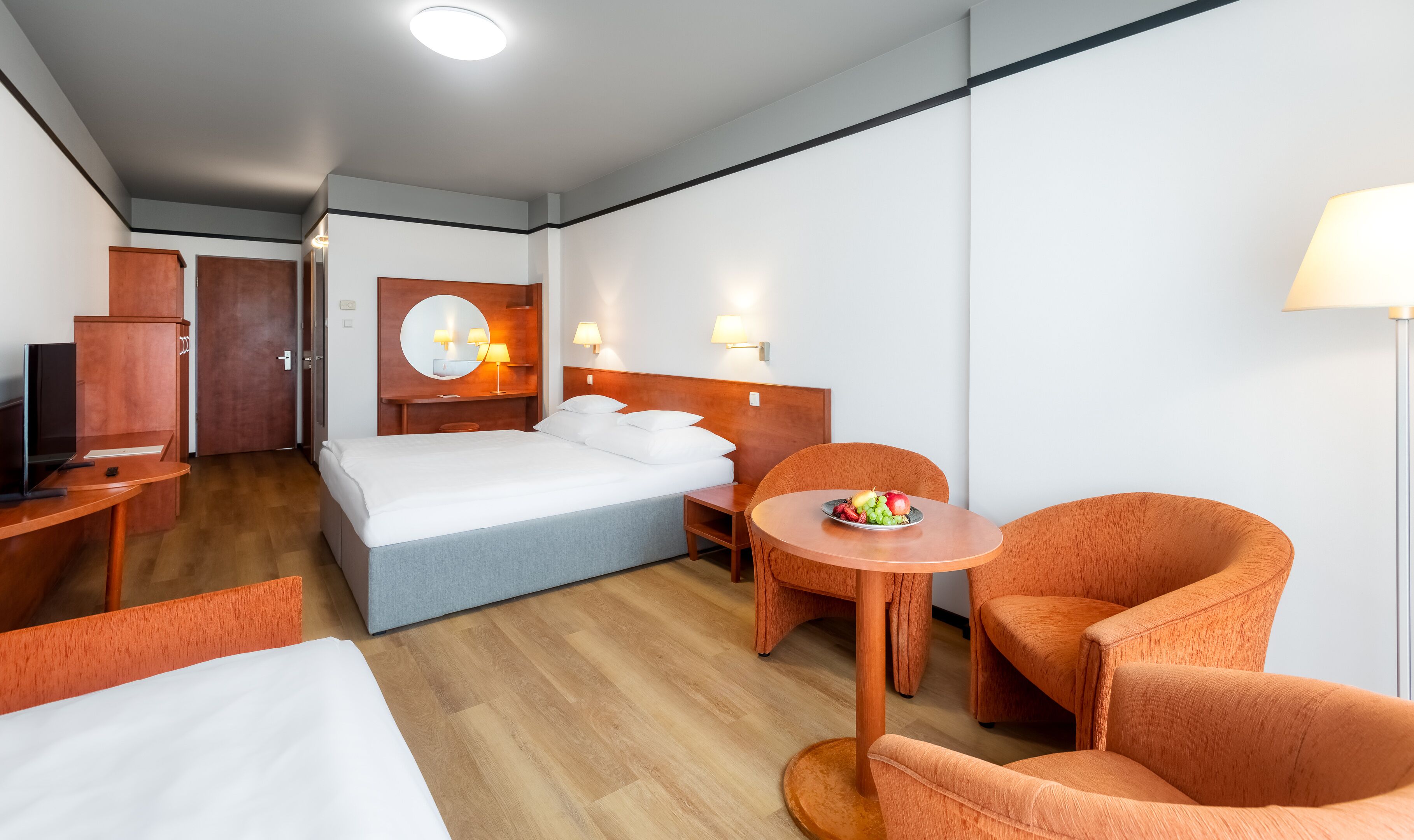Habitación de hotel con cama, escritorio, silla, una pequeña mesa con fruta y una lámpara.