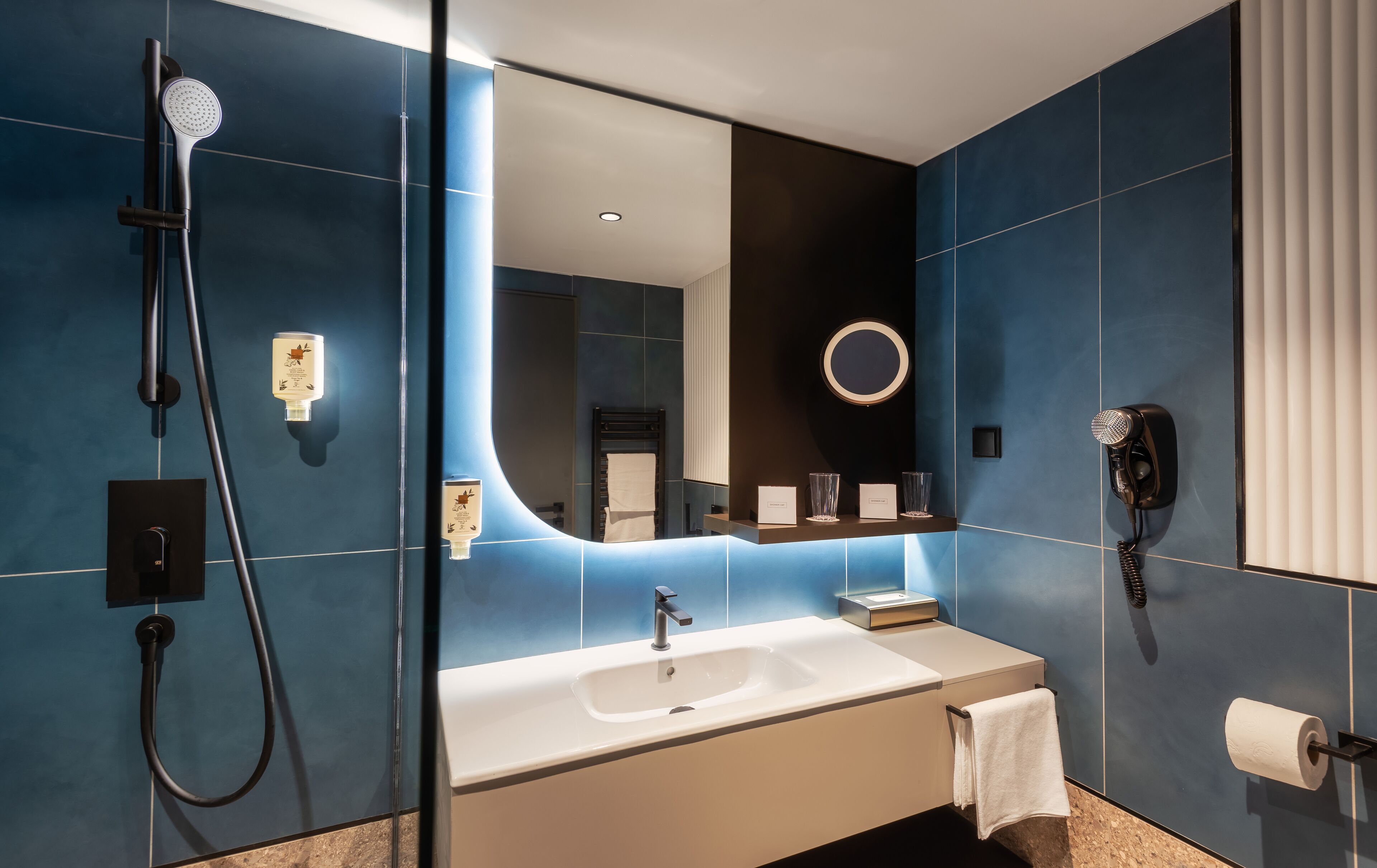 A modern bathroom with a large mirror, a sink, a handheld showerhead, a hairdryer, and a towel rack.