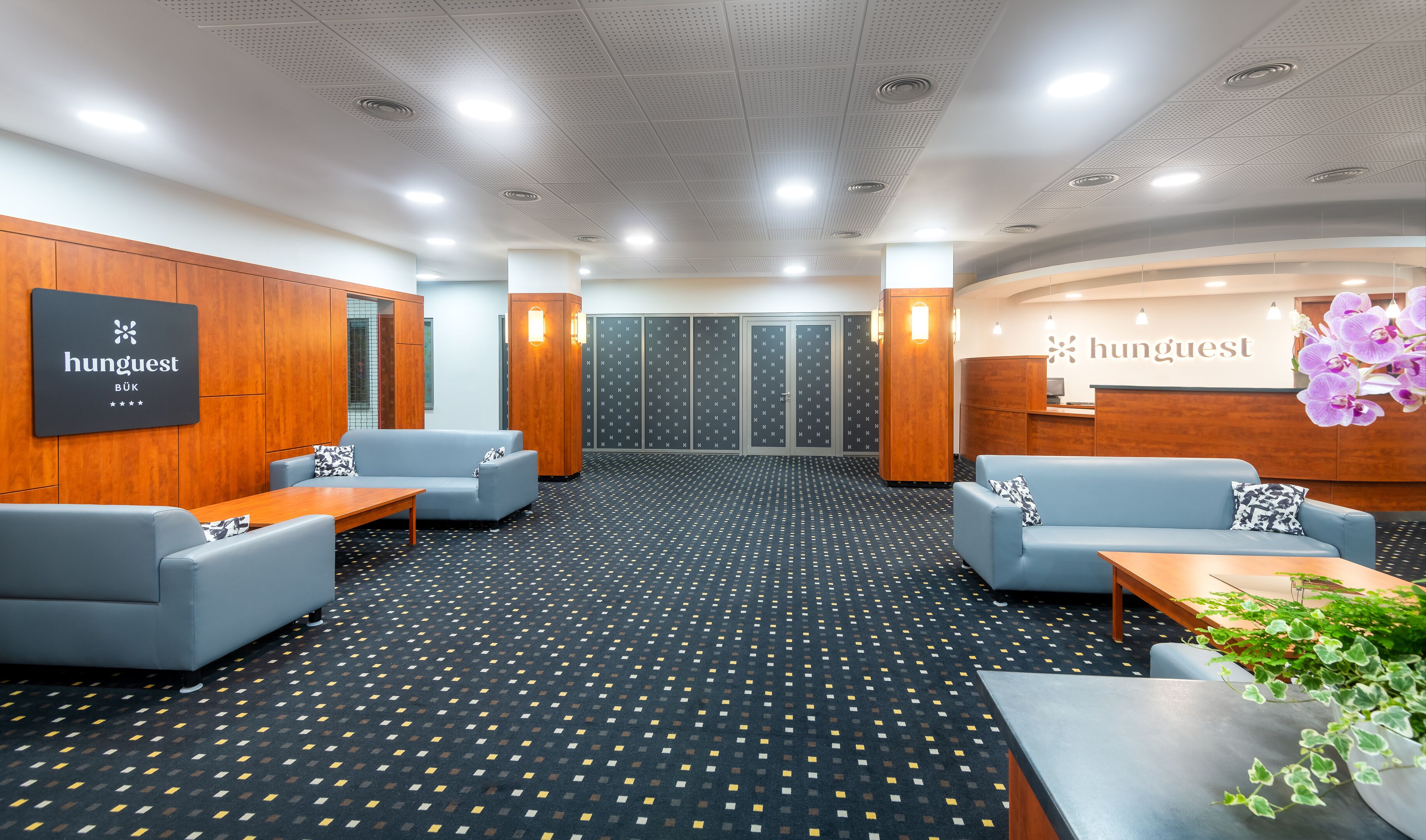 A modern hotel lobby with seating areas, a reception desk, and a patterned floor.