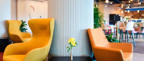 A modern lobby with two yellow armchairs, a black side table, and a vase with yellow flowers.